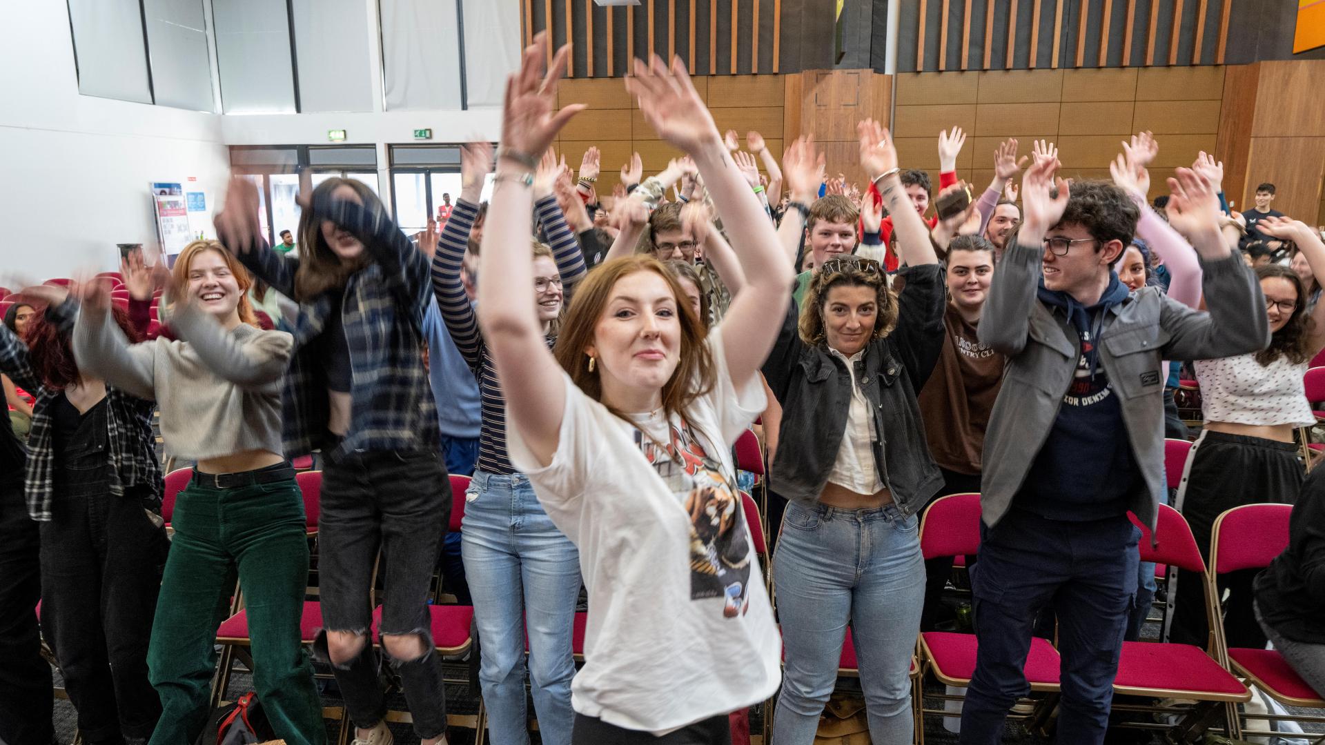 large group of students standing with their hands in their during an orientation activity in the Bailey Allen Hall